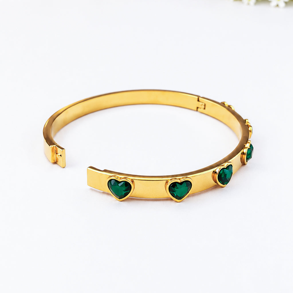 Gold bangle bracelet featuring heart-shaped green crystals