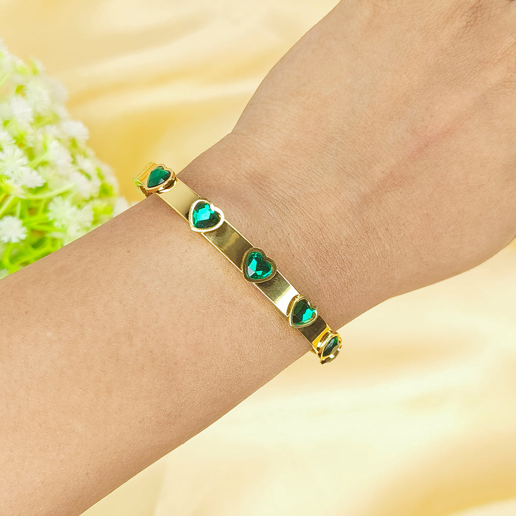 Gold bangle bracelet with inlaid green heart-shaped crystals on a wrist