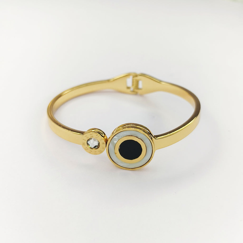Gold bangle bracelet featuring a black and white evil eye charm and a small sparkling crystal.