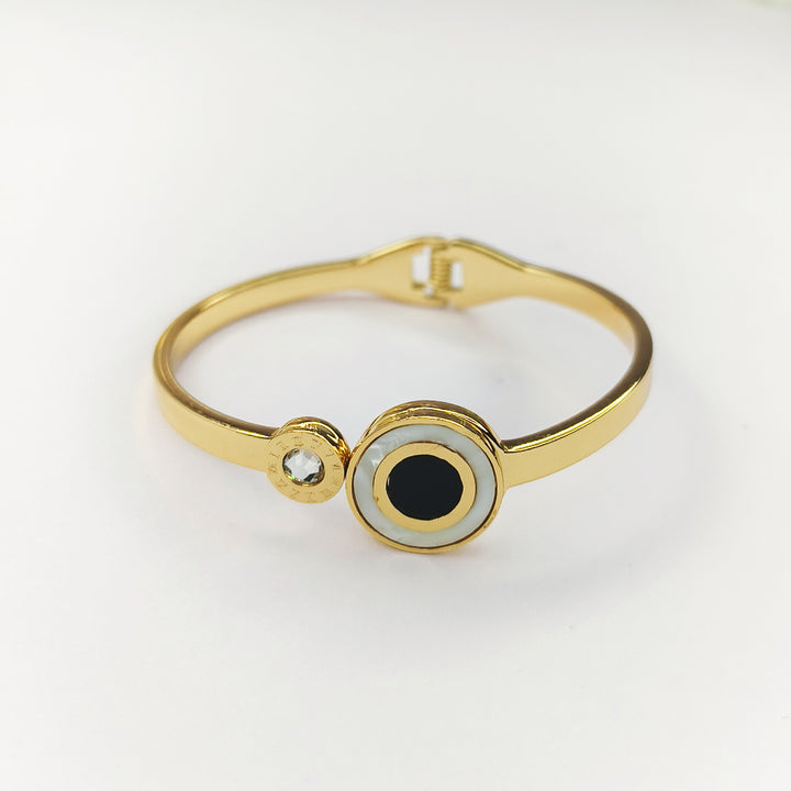 Gold bangle bracelet featuring a black and white evil eye charm and a small sparkling crystal.