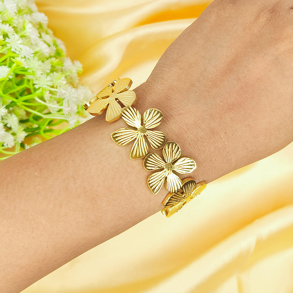Gold-plated flower-shaped link bracelet worn on a wrist against a yellow silk background