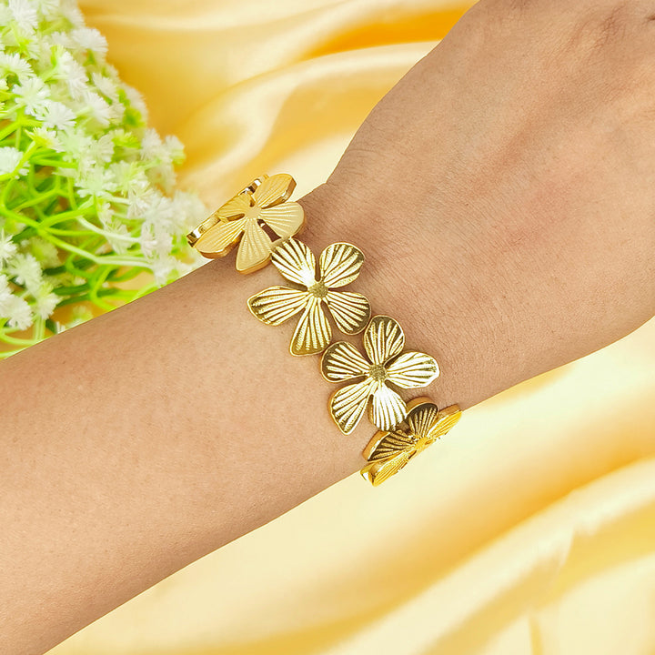 Gold-plated flower-shaped link bracelet worn on a wrist against a yellow silk background