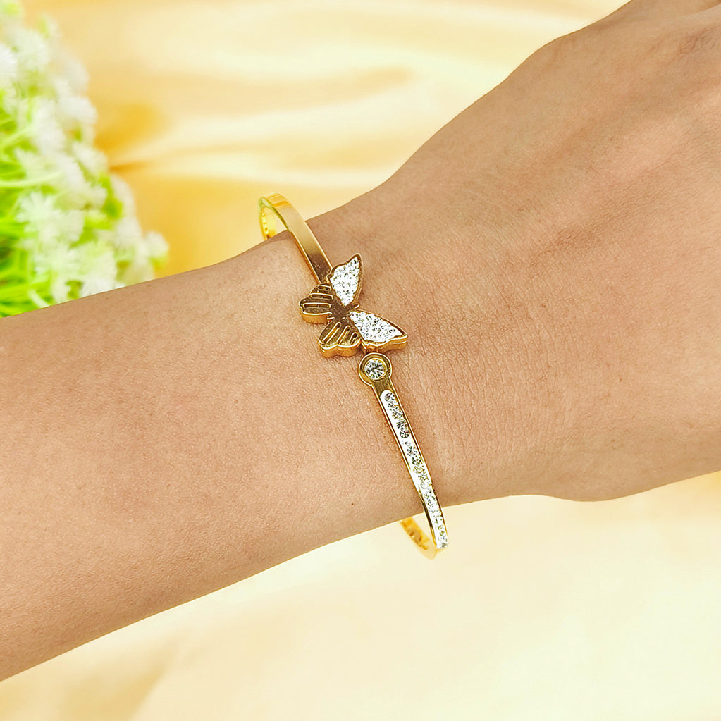 Gold-plated bangle bracelet with a diamond-studded butterfly design on a wrist