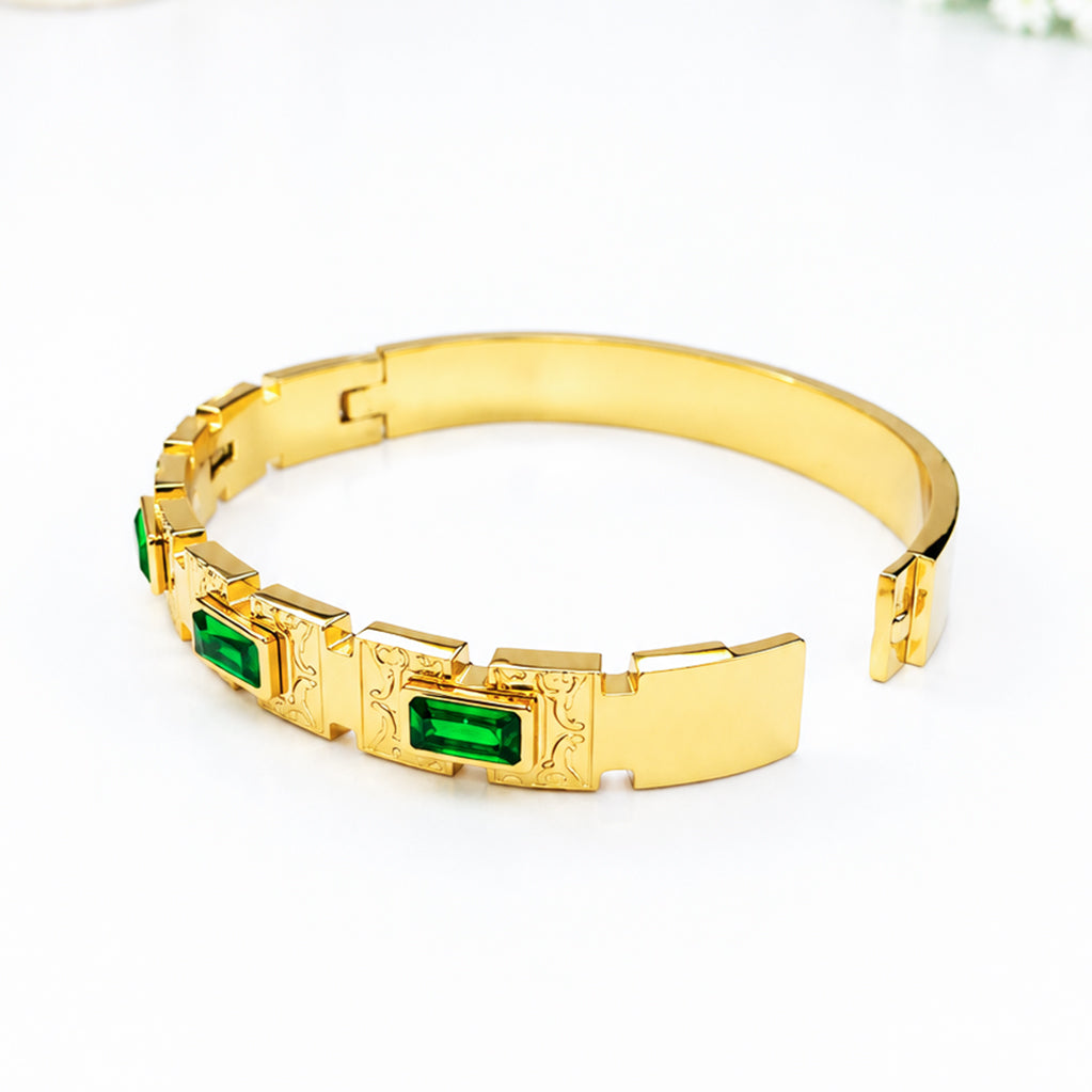 Gold bangle bracelet with emerald green rectangular gemstones and ornate engravings