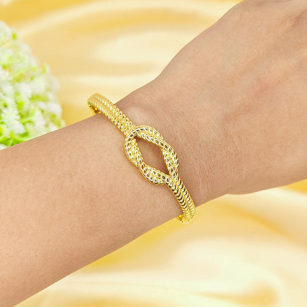 Elegant gold twisted knot bangle worn on a woman's wrist against a yellow silk background.