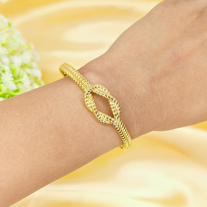 Elegant gold twisted knot bangle worn on a woman's wrist against a yellow silk background.