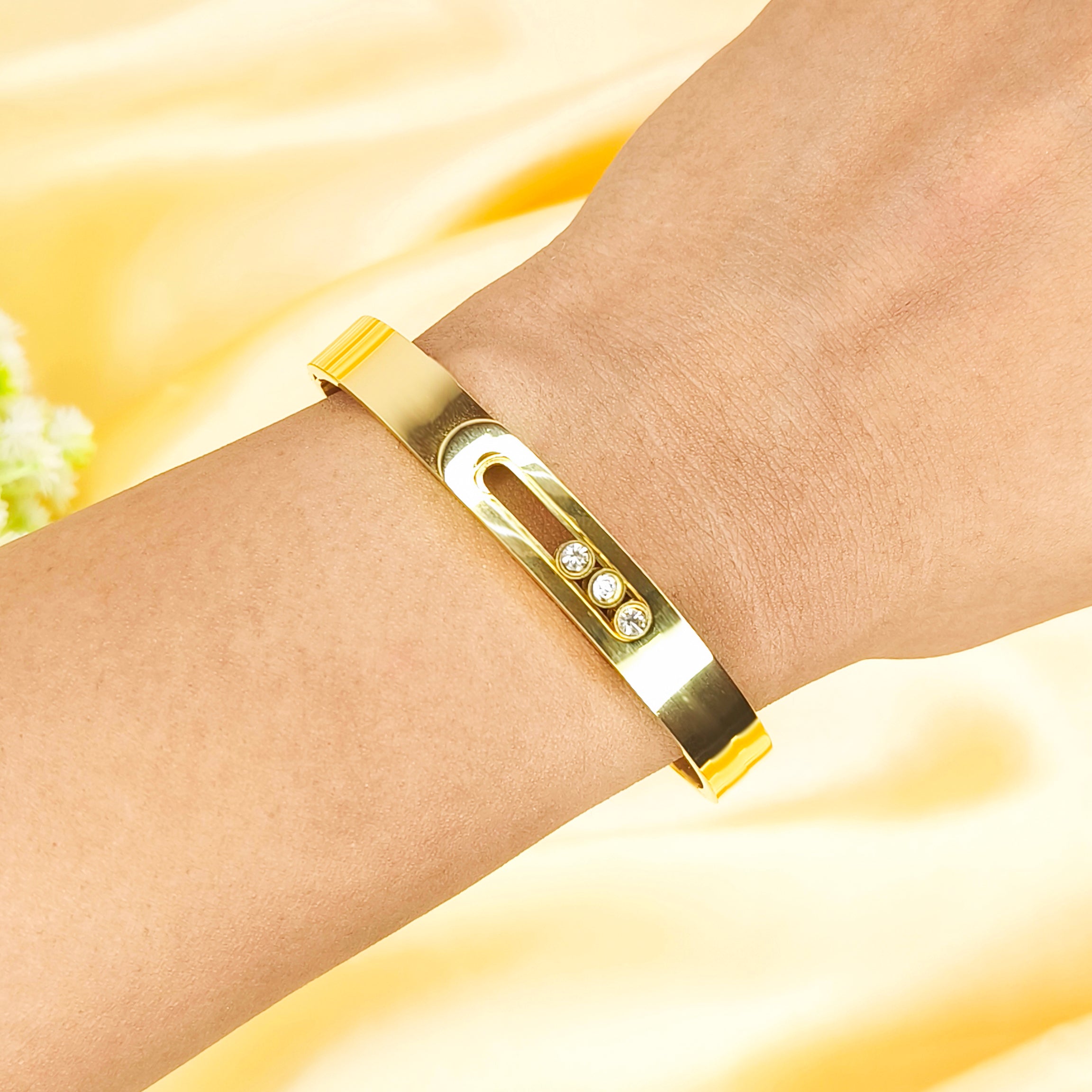 Elegant gold bangle bracelet with three inlaid clear gemstones worn on a wrist.
