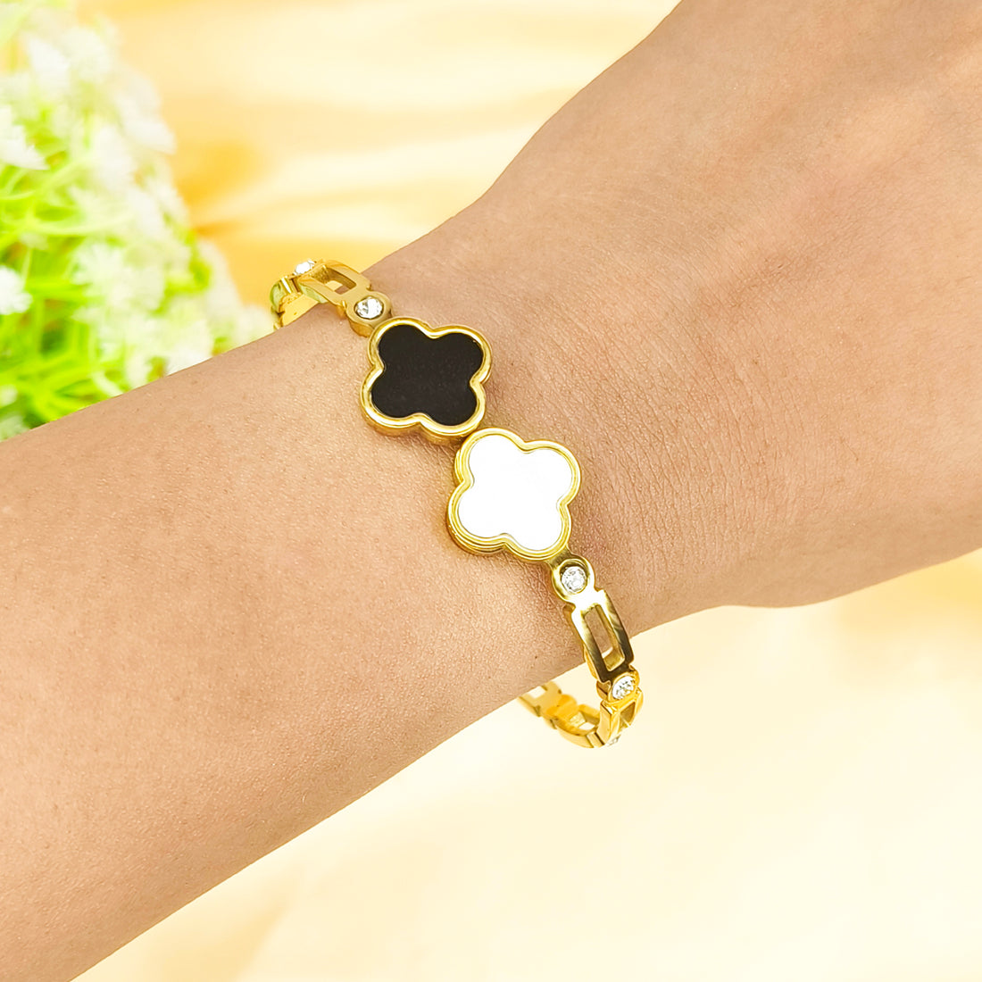 Gold clover bracelet with black and white enamel quatrefoil charms on a wrist