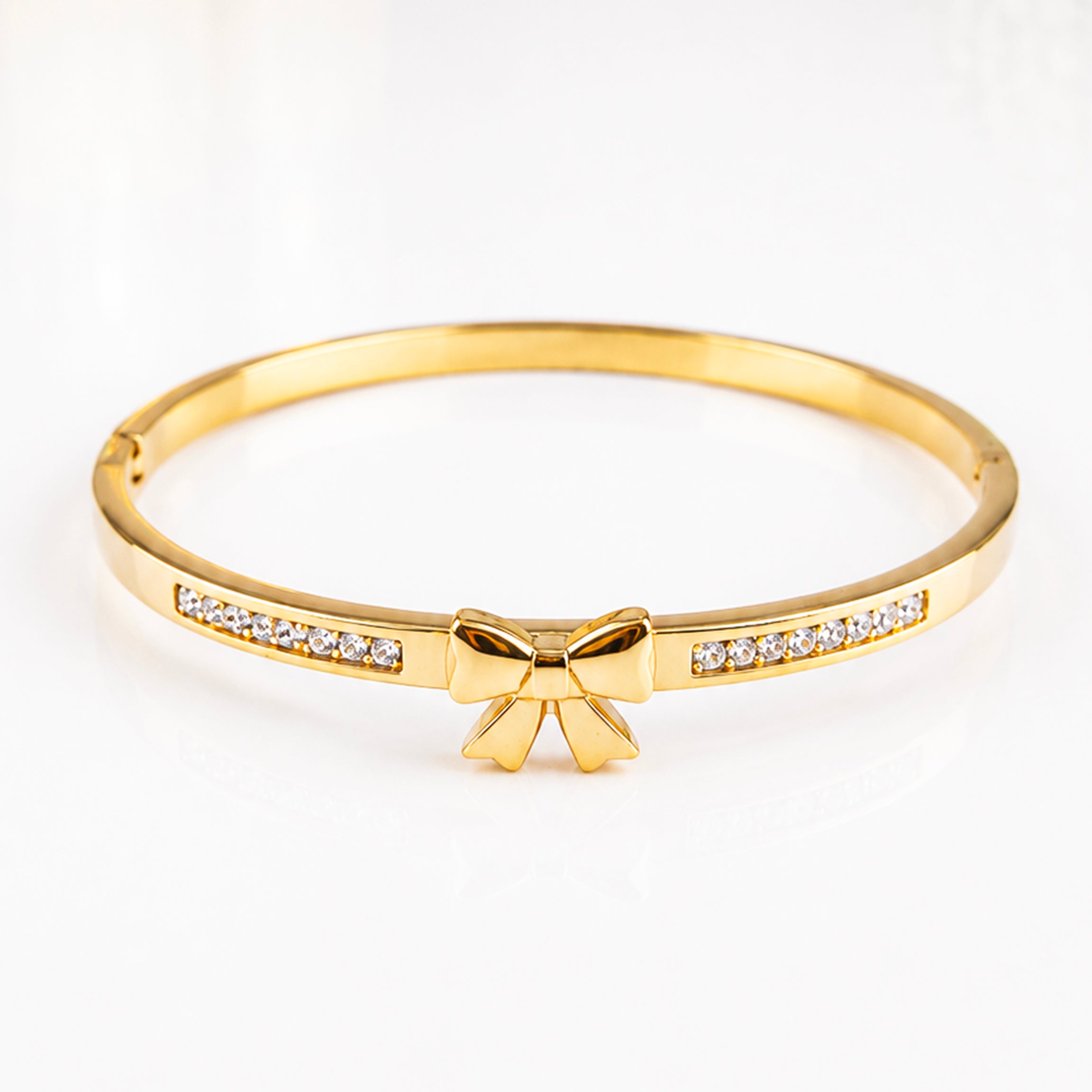 Elegant gold bangle bracelet featuring a bow charm and sparkling inlaid crystals.