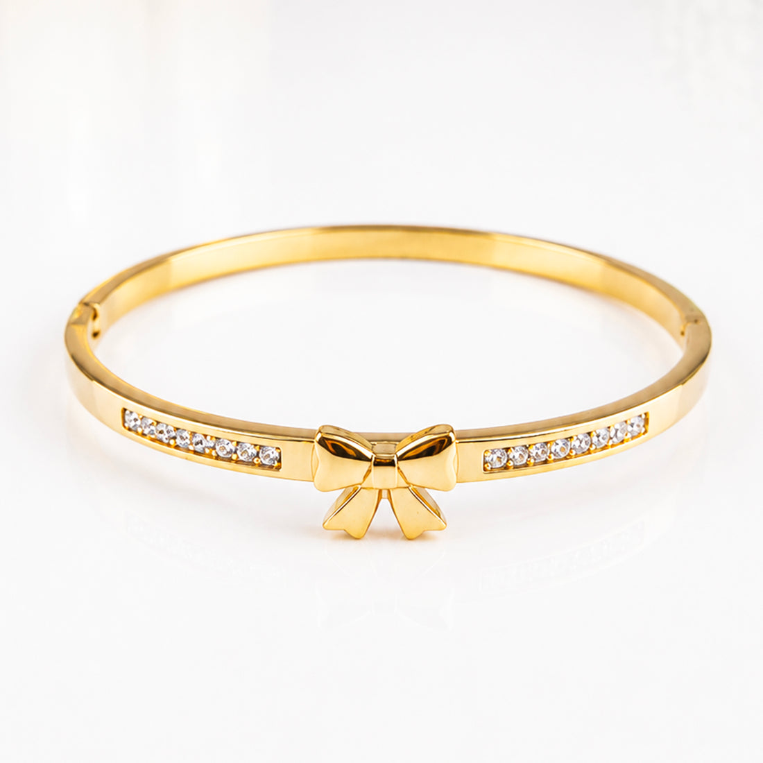 Elegant gold bangle bracelet featuring a bow charm and sparkling inlaid crystals.