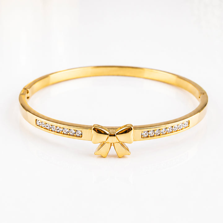 Elegant gold bangle bracelet featuring a bow charm and sparkling inlaid crystals.