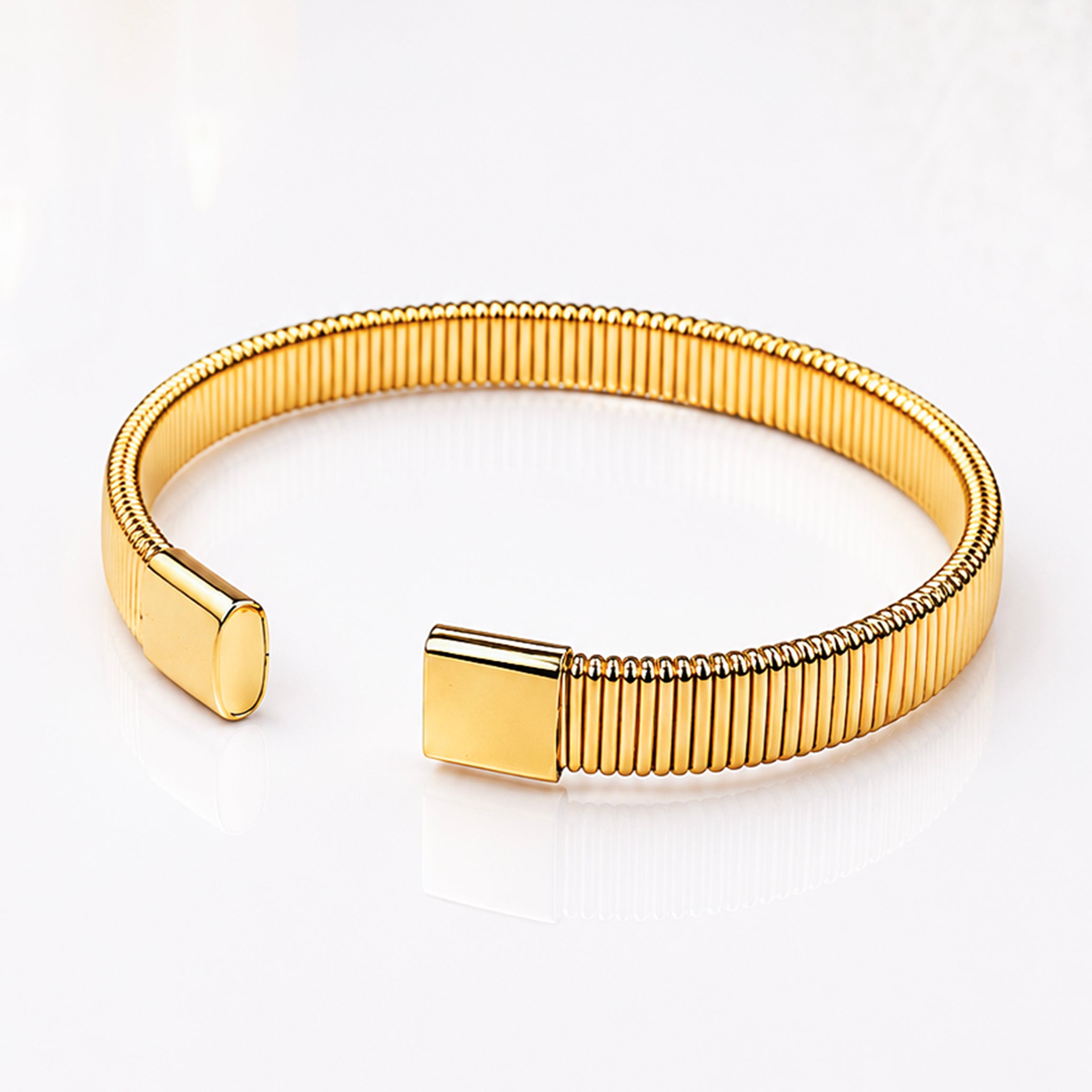 Elegant gold ribbed bangle bracelet with polished smooth end caps on a white reflective surface.