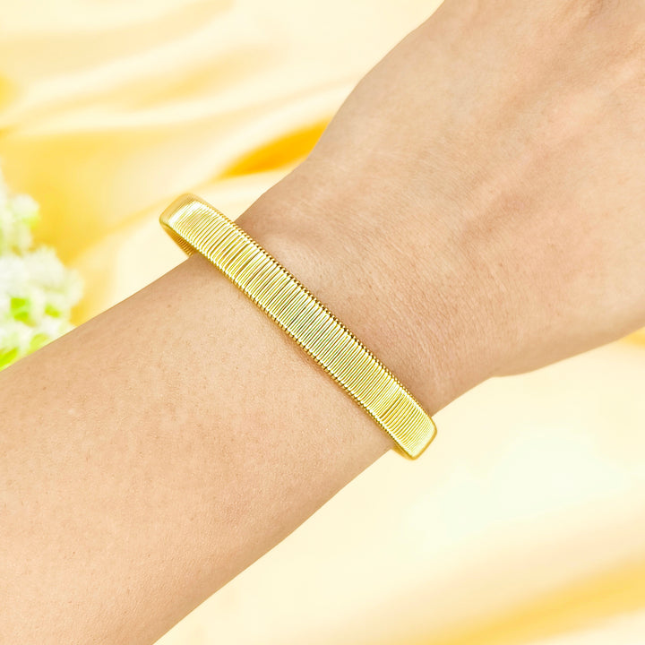 Elegant gold textured bangle bracelet worn on a woman's wrist against a yellow background.