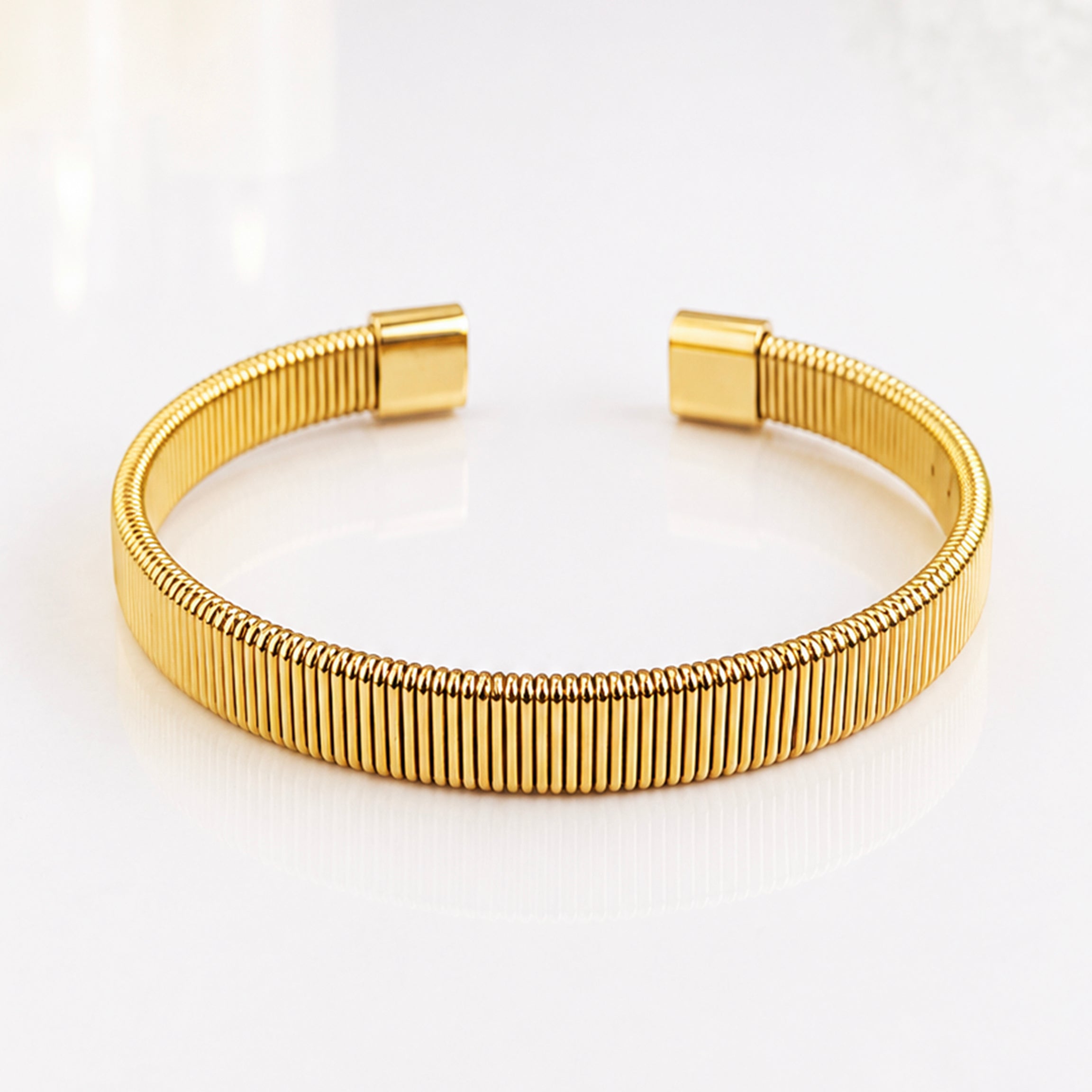 Elegant gold ribbed bangle bracelet on a white reflective surface