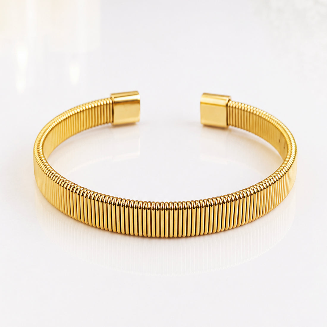 Elegant gold ribbed bangle bracelet on a white reflective surface