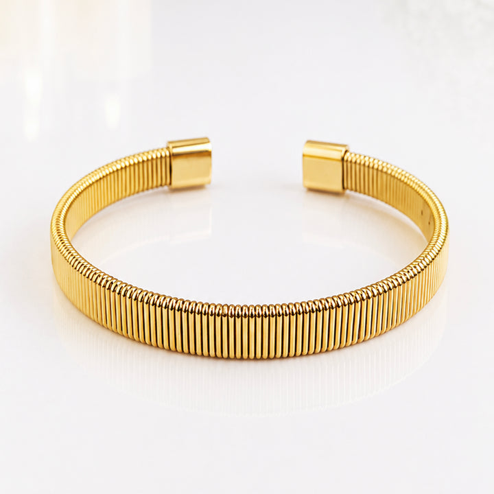 Elegant gold ribbed bangle bracelet on a white reflective surface
