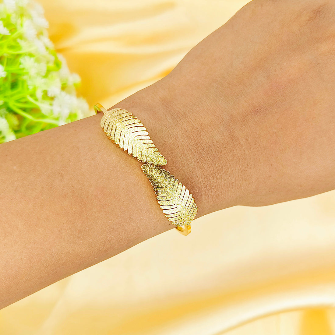 Gold leaf design bangle bracelet worn on a wrist against a yellow silk background