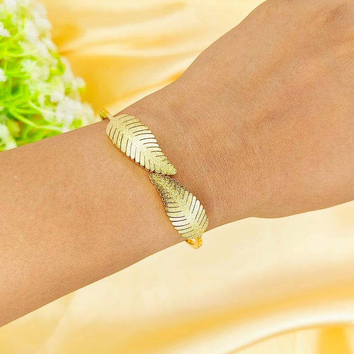 Gold leaf design bangle bracelet worn on a wrist against a yellow silk background