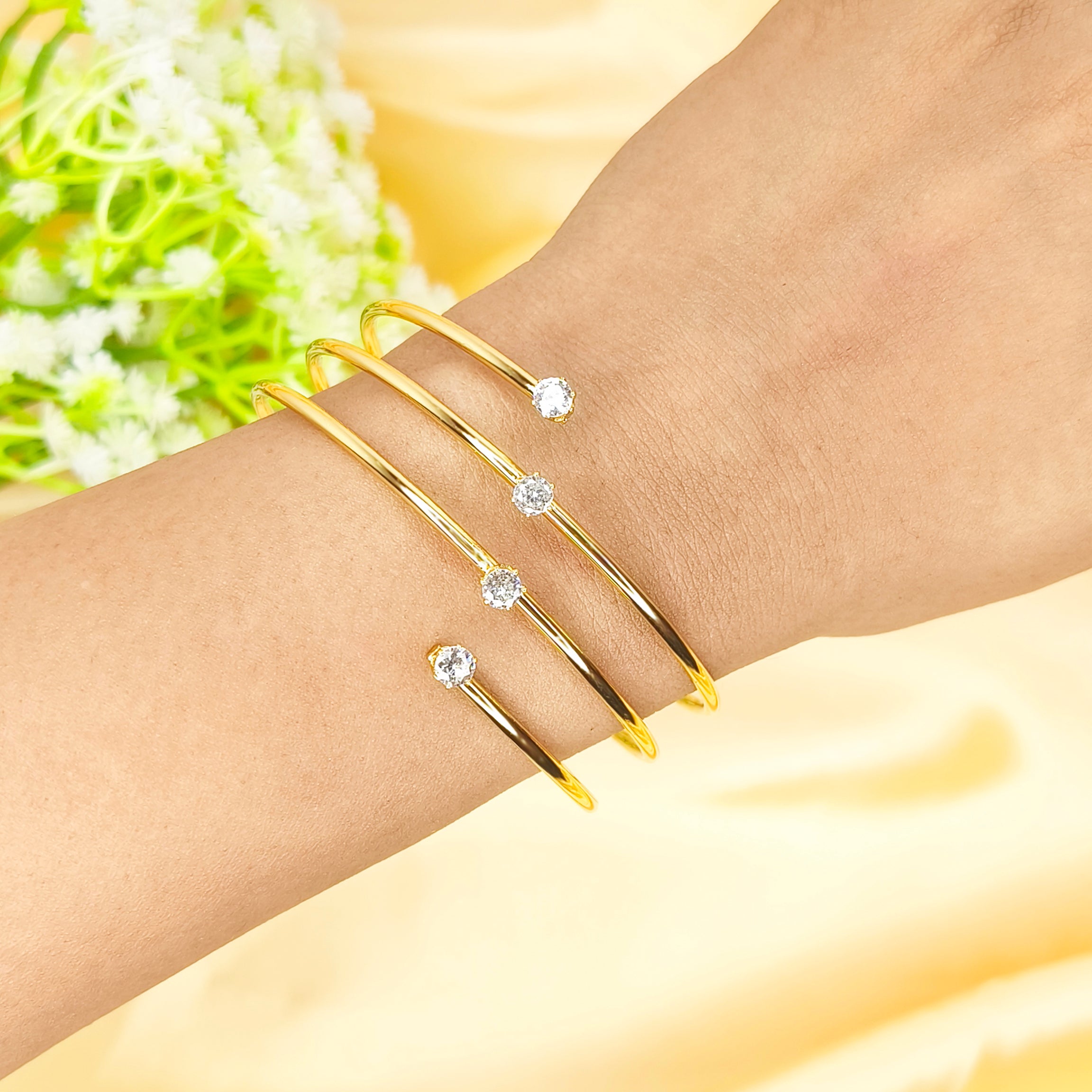 Set of four gold-plated open bangles with sparkling cubic zirconia crystals on a wrist