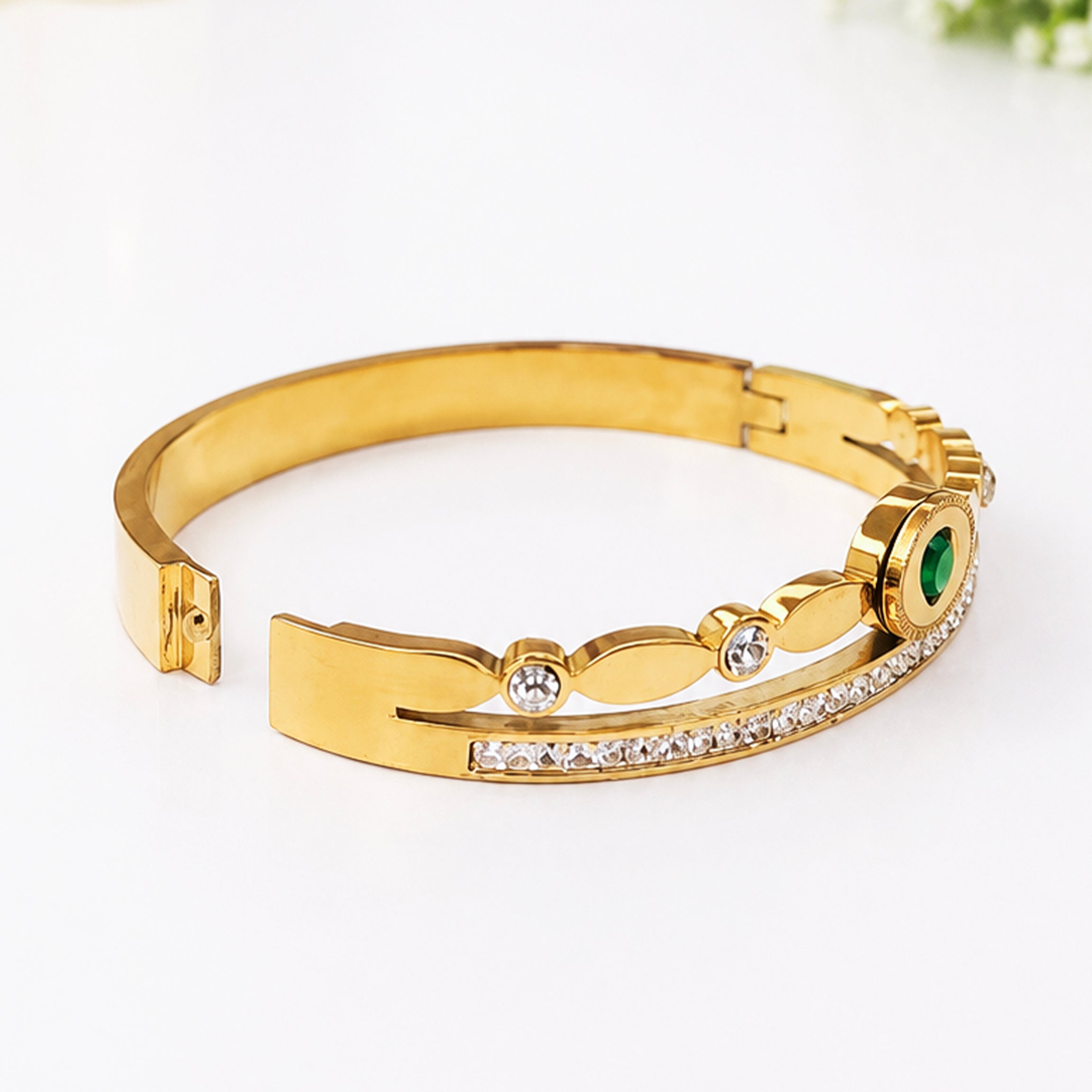 Gold-plated bangle bracelet with clear crystals and a center green gemstone