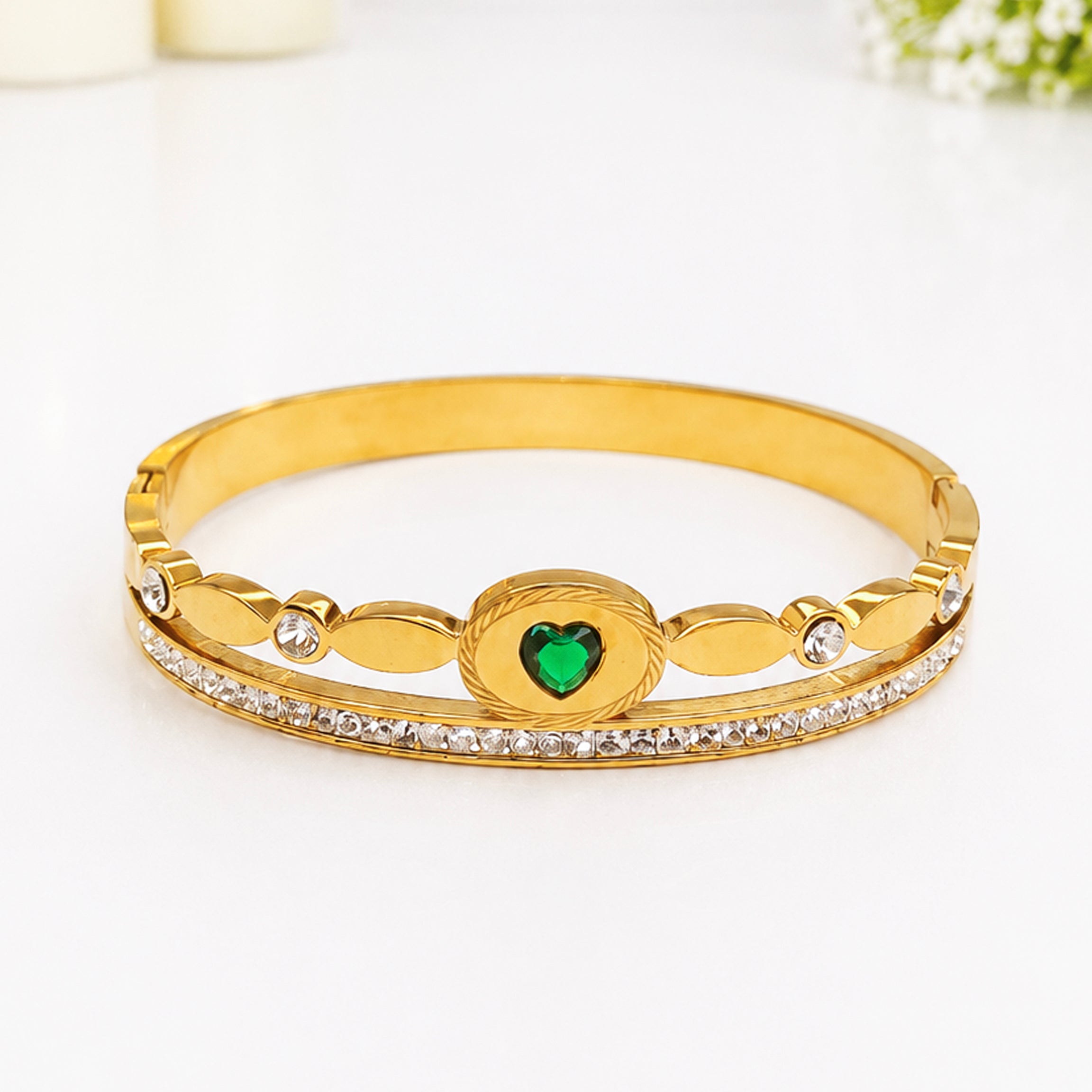 Gold-toned bangle bracelet with a heart-shaped green gemstone and sparkling crystals