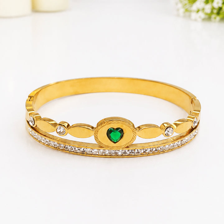 Gold-toned bangle bracelet with a heart-shaped green gemstone and sparkling crystals