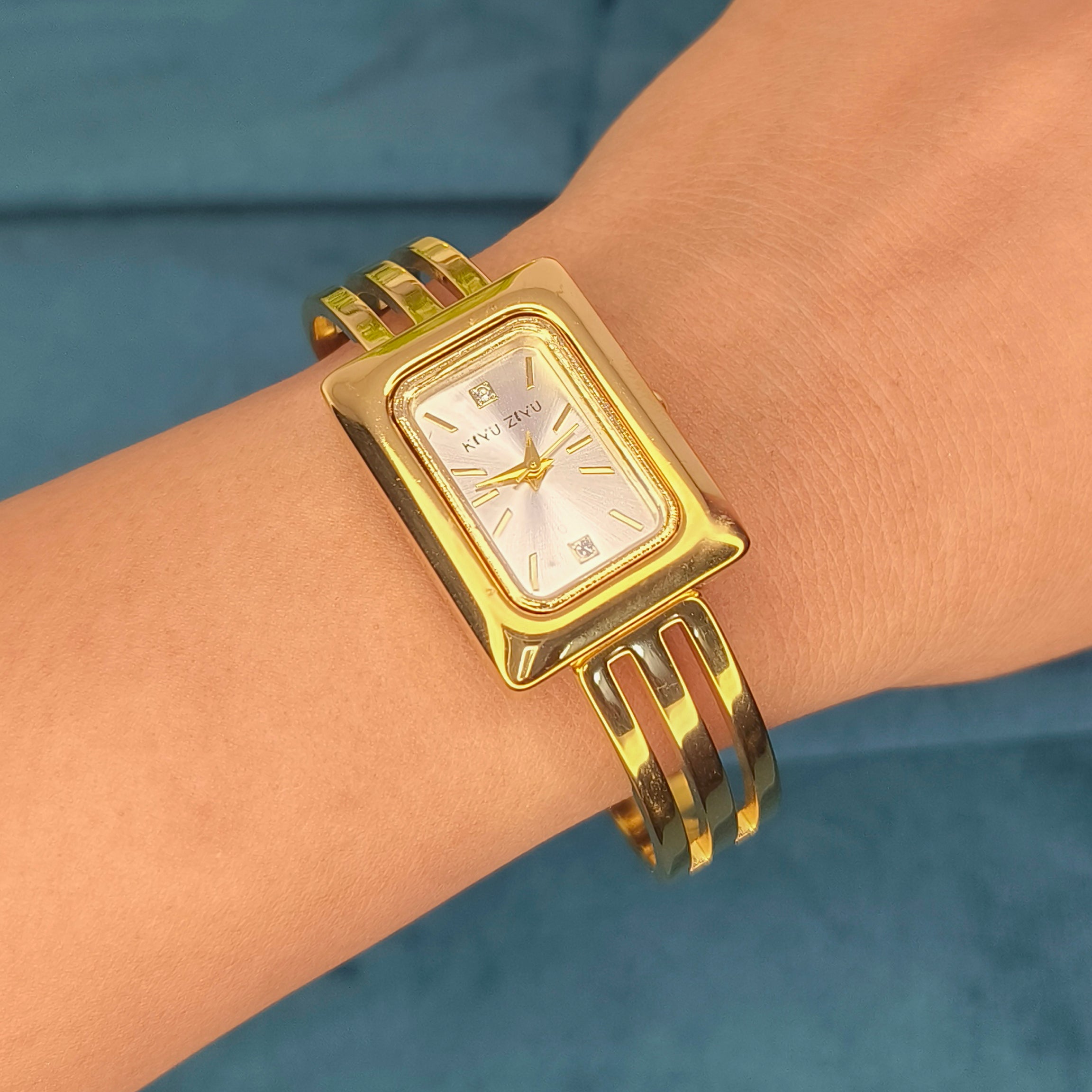 Elegant gold rectangular face wristwatch with a metallic link bracelet worn on a wrist.