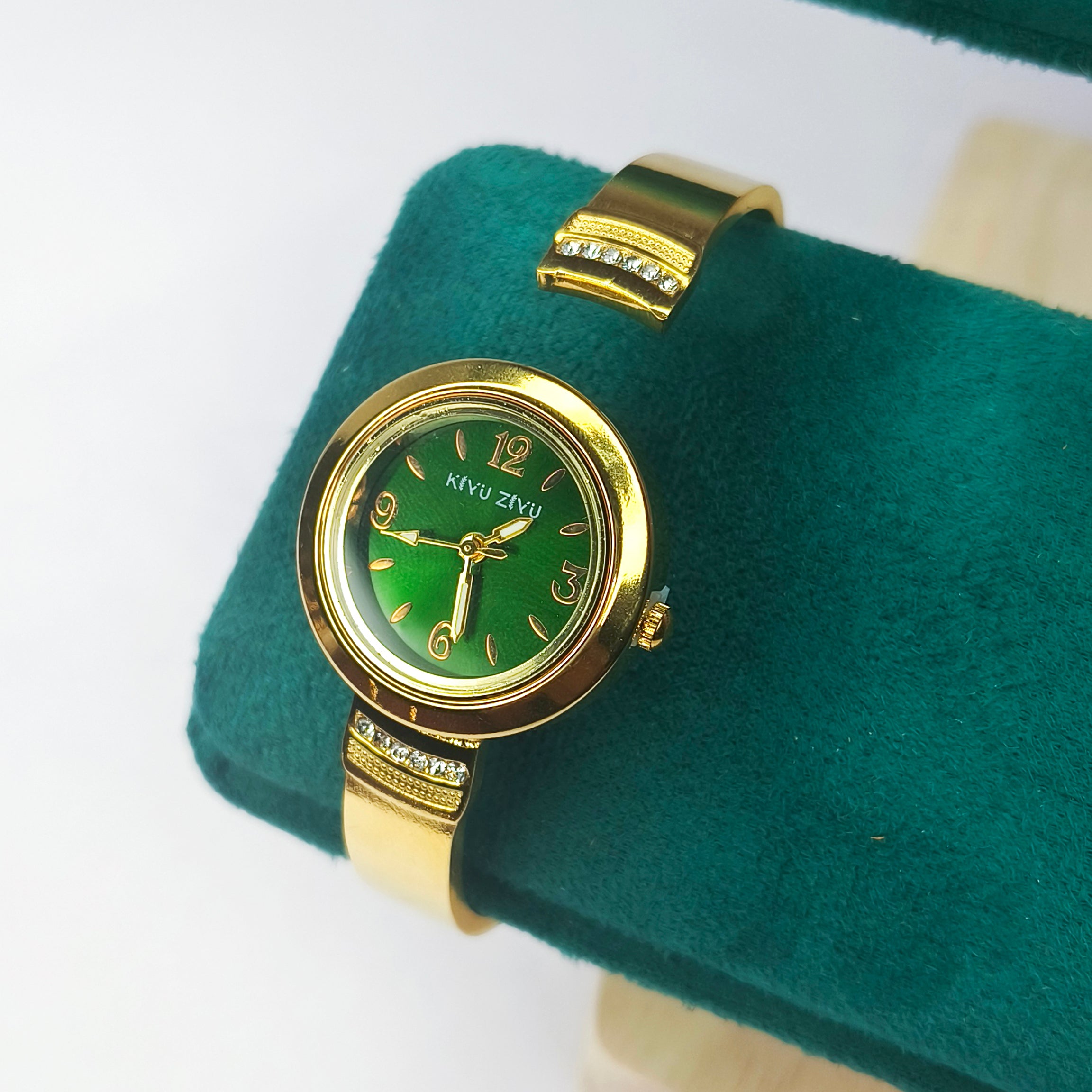 Elegant gold women's watch with a green dial and crystal-embellished band on a green velvet cushion.