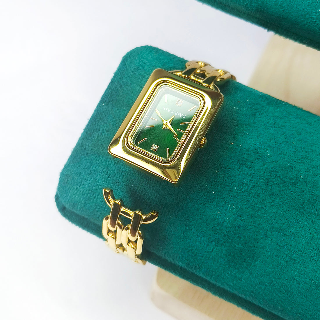 Elegant gold rectangular women's watch with a green dial on a teal velvet cushion