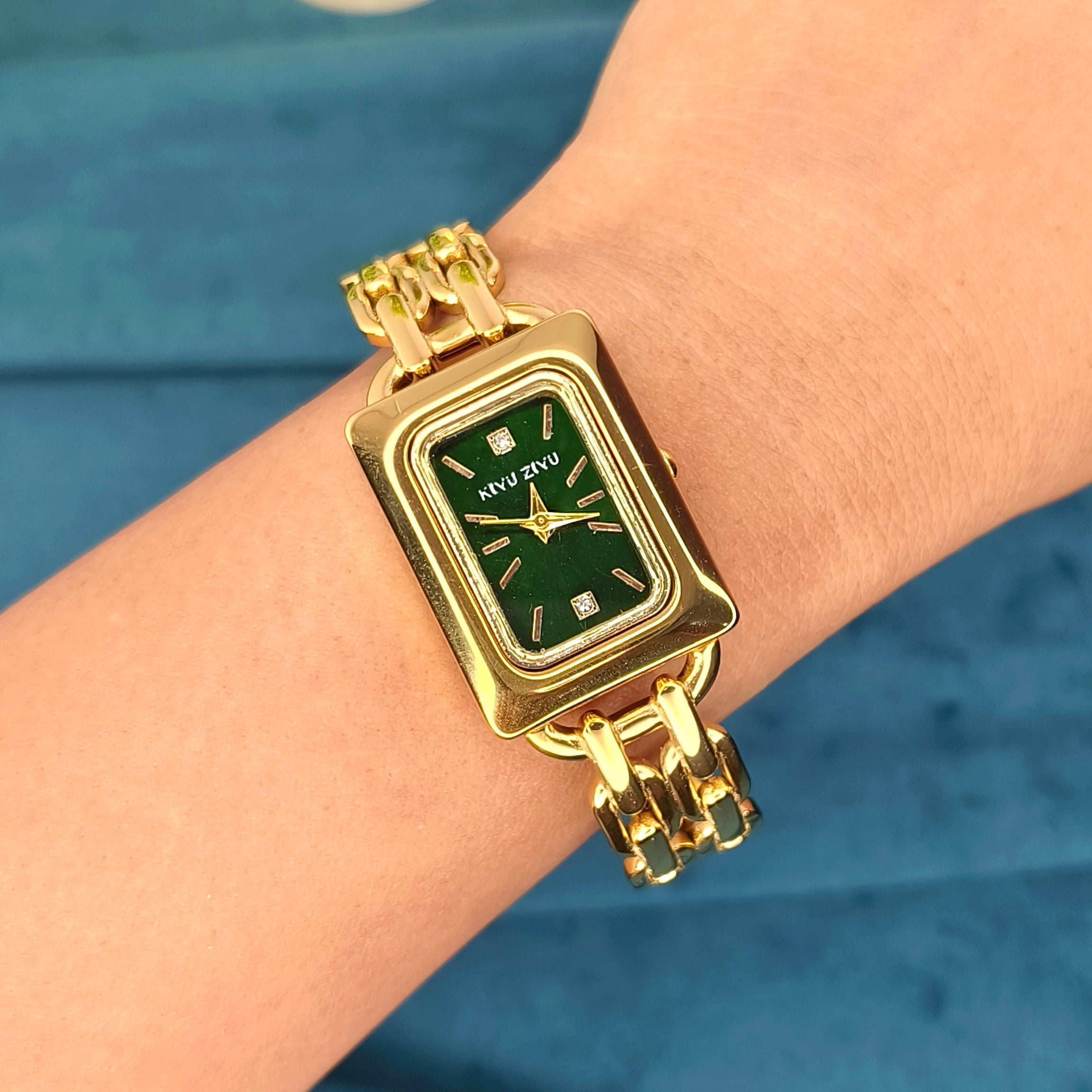 Gold rectangular luxury watch with green dial worn on a wrist